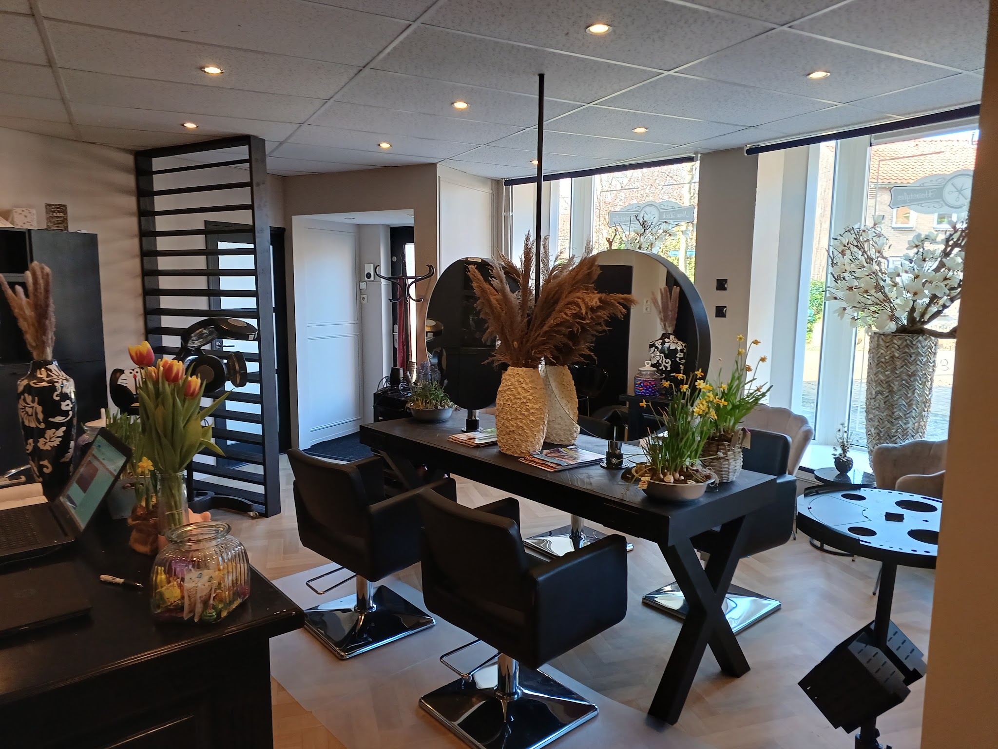 De salon met zwarte kaptafel, ronde spiegels, pampasgras en grote ramen